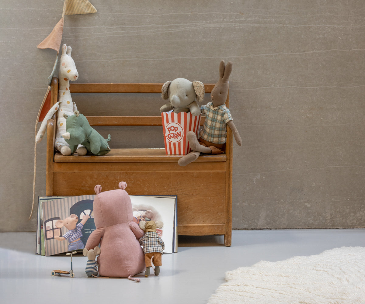 Children's toys, including a pink bear and elephant, on a wooden bench against a plain wall.