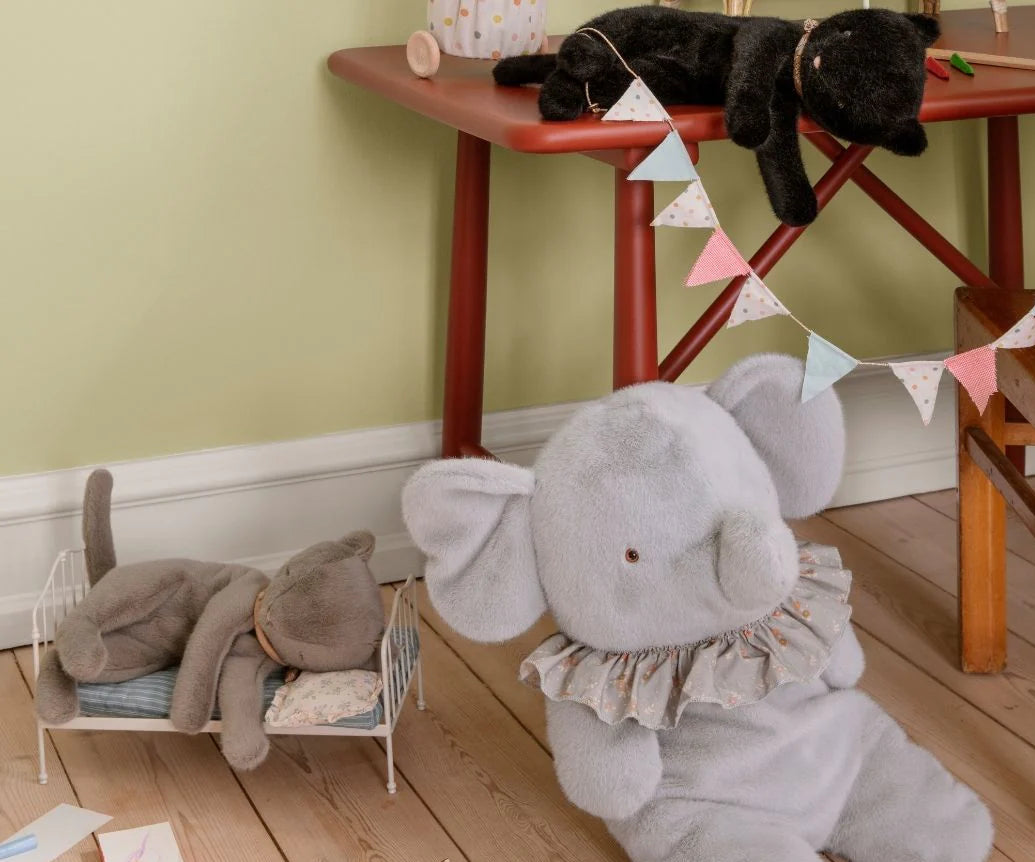 Children's room with a large gray elephant plush toy on the floor, a small dollhouse, and a black cat on a red table.