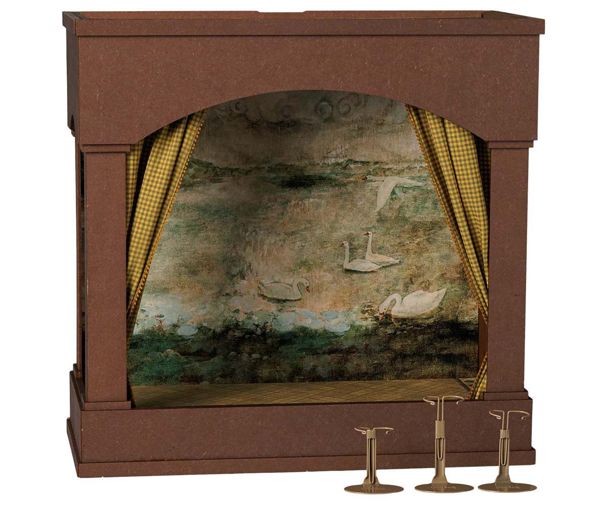 A miniature dollhouse stage set featuring a brown wooden archway backdrop with a painted swan pond scene inside, flanked by gold checkered curtains, with three brass bell stands on a white background.