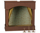 A miniature dollhouse-style fireplace or stage opening with a brown frame, patterned green and gold damask wallpaper, gold checkered curtains, and three small gold pedestal accessories on a white background.