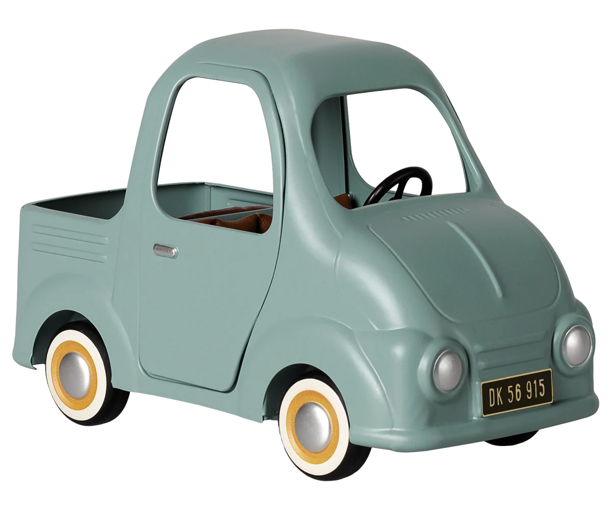 A retro-style toy pickup truck in a muted sage green color, featuring yellow-rimmed white wheels, a black steering wheel, and a small license plate reading 'DK 56 915'.