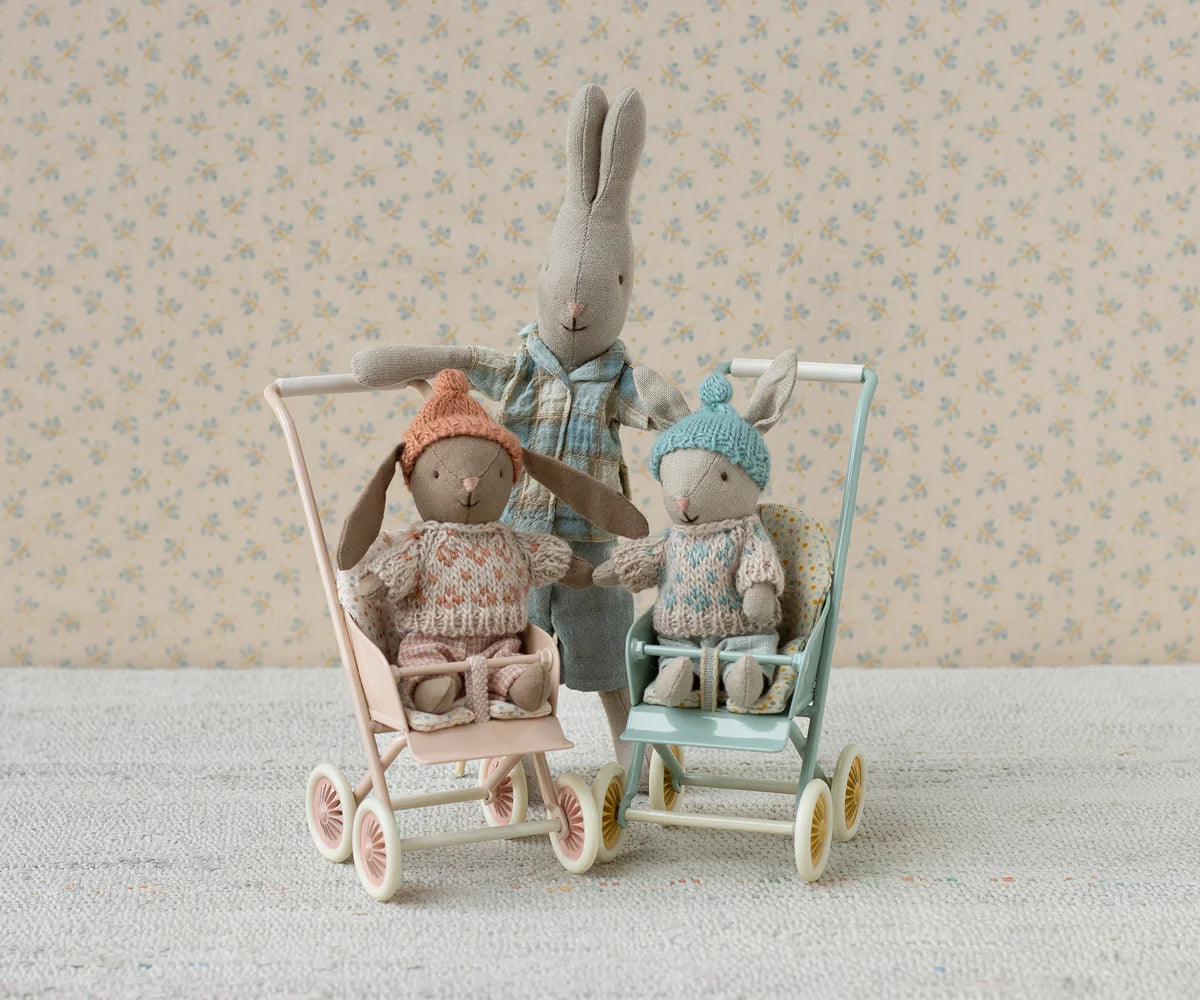Two stuffed animals in toy strollers with a floral wallpaper background