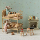 A miniature dollhouse-style room scene with two plush mouse figures arranged on a wooden bunk bed, alongside small furniture pieces, a wallpapered wall, and a fireplace display.