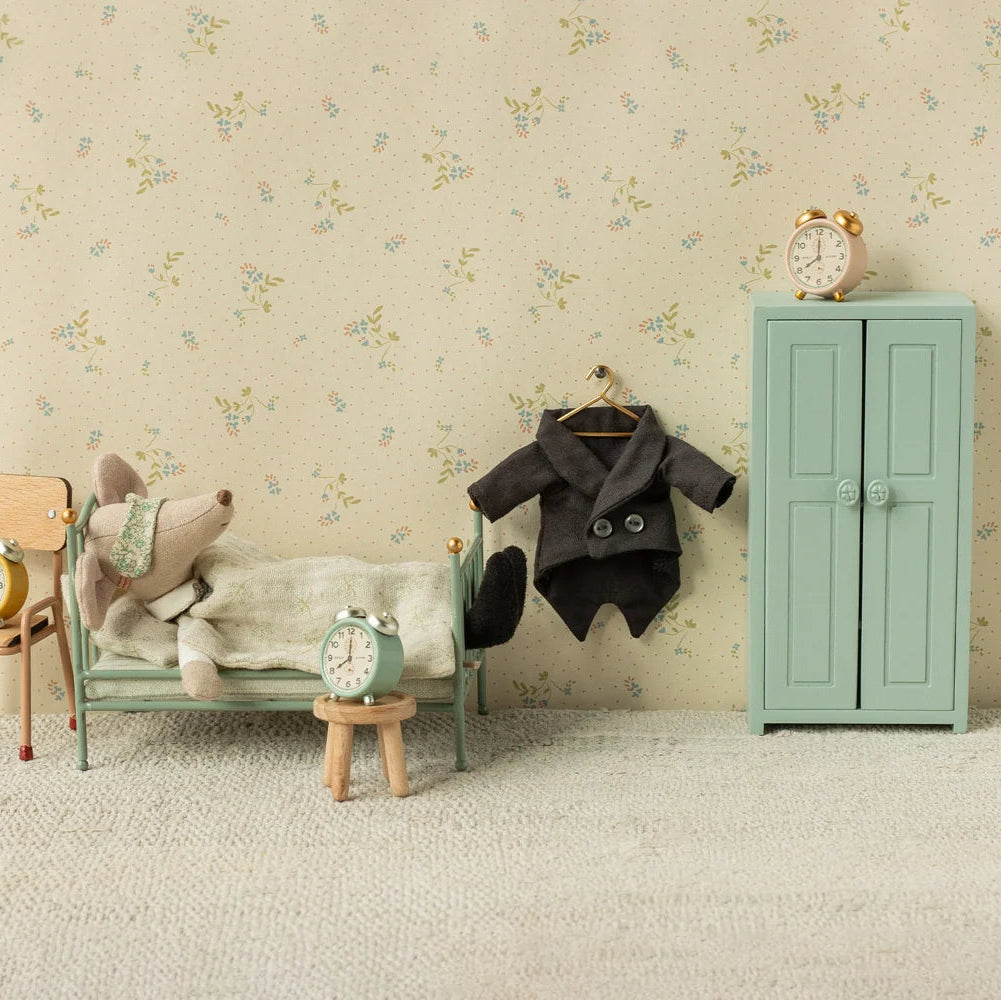 MAileg Miniature bedroom setup with a bed, chair, coat, and wardrobe against a floral wallpapered wall.