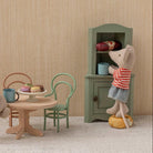 Miniature Maileg scene with toy mice around a table in a room with striped wallpaper.