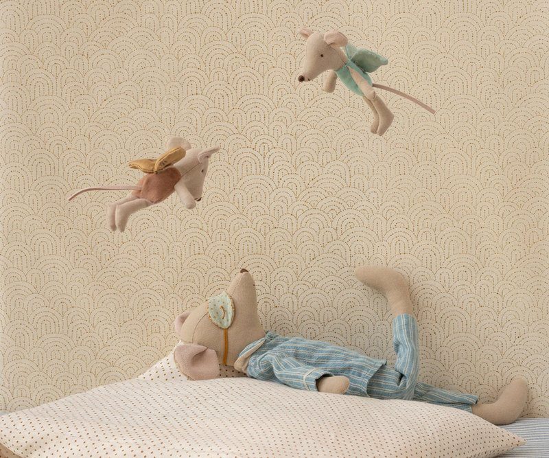 Stuffed Maileg maxi slze mouse in pyjamas lying on a bed with decorative wallpaper in the background and two maileg fairies flying above 
