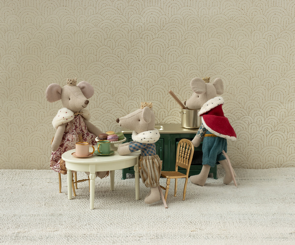 Maileg king queen and prince mice  sitting around a small table against a patterned wall.