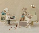 Three toy Maileg mice in a kitchen setting with a patterned wallpaper background.