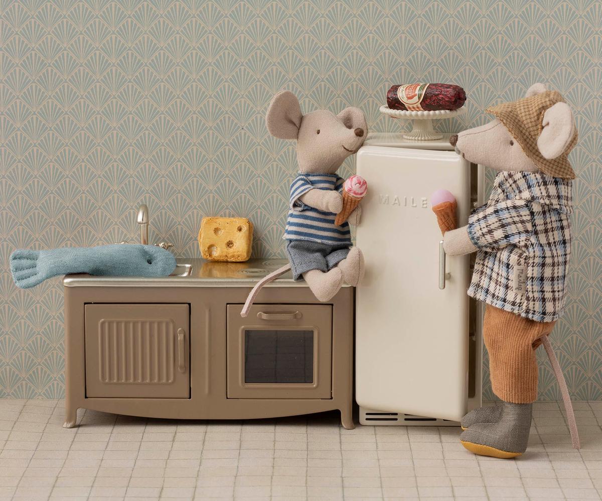 Two toy mice in a kitchen setting with a refrigerator and sink.