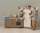 Two toy mice in a kitchen setting with a refrigerator and sink.