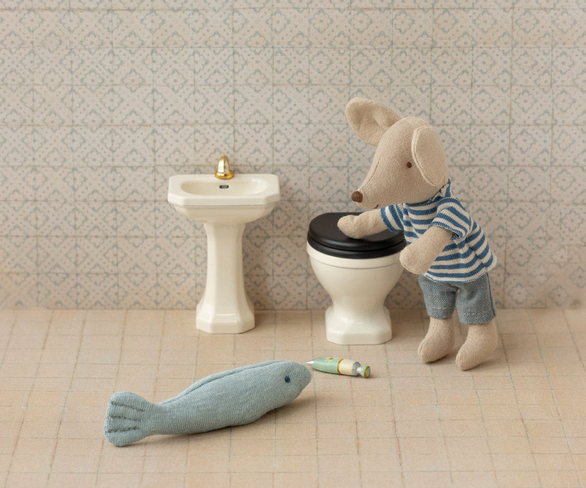 Miniature mouse character using a toy toilet with a fish and cigarette nearby, set against a tiled bathroom wall.