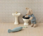 Miniature mouse character using a toy toilet with a fish and cigarette nearby, set against a tiled bathroom wall.
