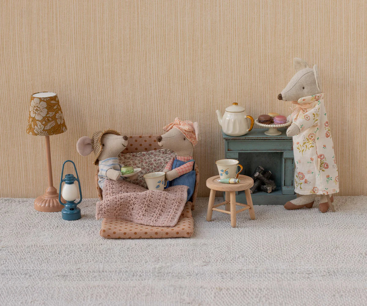 Miniature scene with toy mice and tea set against a beige wall.