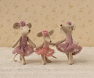 Three toy Maileg mice in ballerina dresses standing on a textured surface with a floral-patterned wall in the background.
