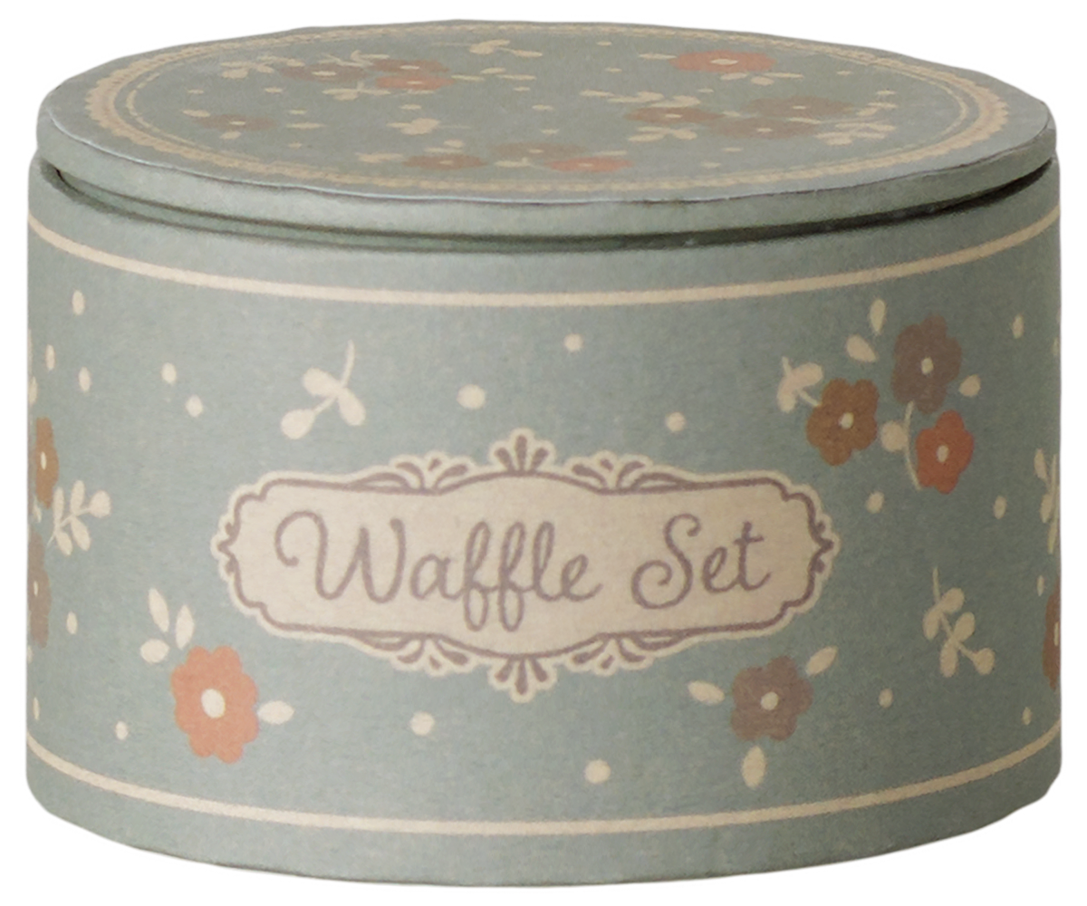 A round lidded tin container for a waffle set, decorated with a dusty sage green background, cream borders, and small orange and brown floral motifs. The front features a cream label with the words 'Waffle Set' in brown script.