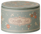 A round lidded tin container for a waffle set, decorated with a dusty sage green background, cream borders, and small orange and brown floral motifs. The front features a cream label with the words 'Waffle Set' in brown script.