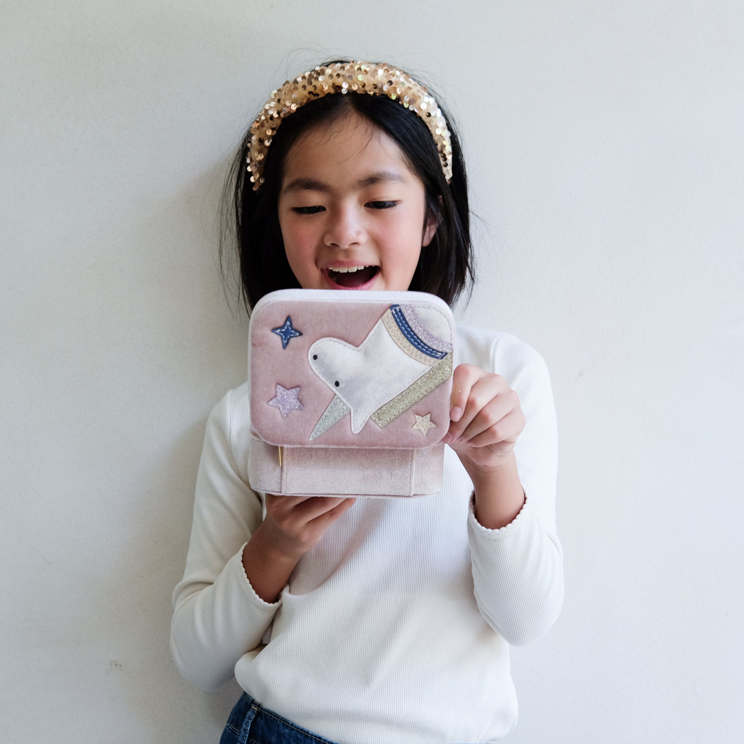 Child holding a pink unicorn jewellery box  against a plain background