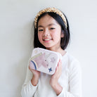 Young girl holding a jewellery box with a unicorn design against a plain background