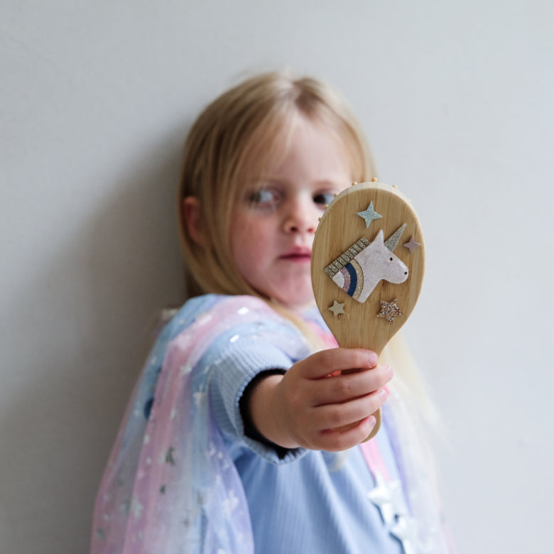 Child holding a wooden brush with a unicorn design against a plain background