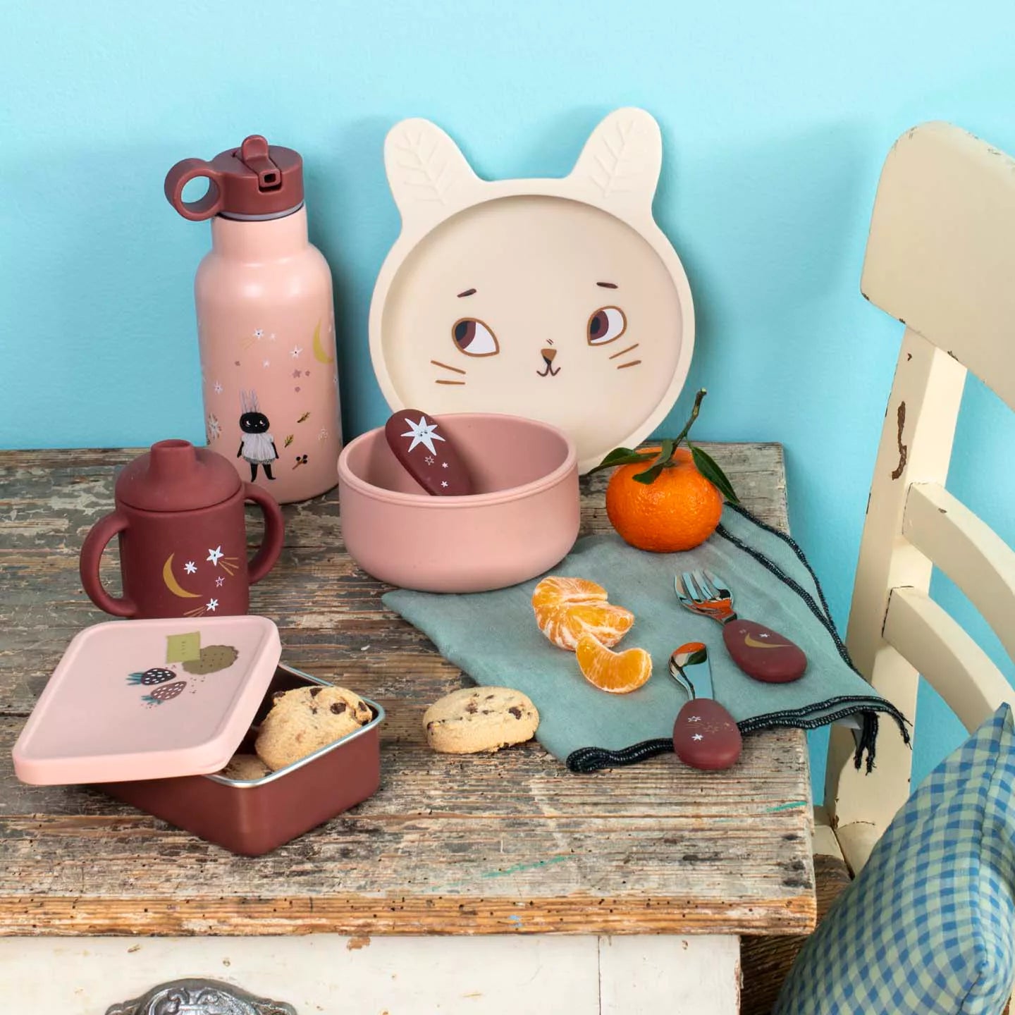 Children's table setting with pink and red dish,  water bottle, and a plate with cat ears on a blue background.