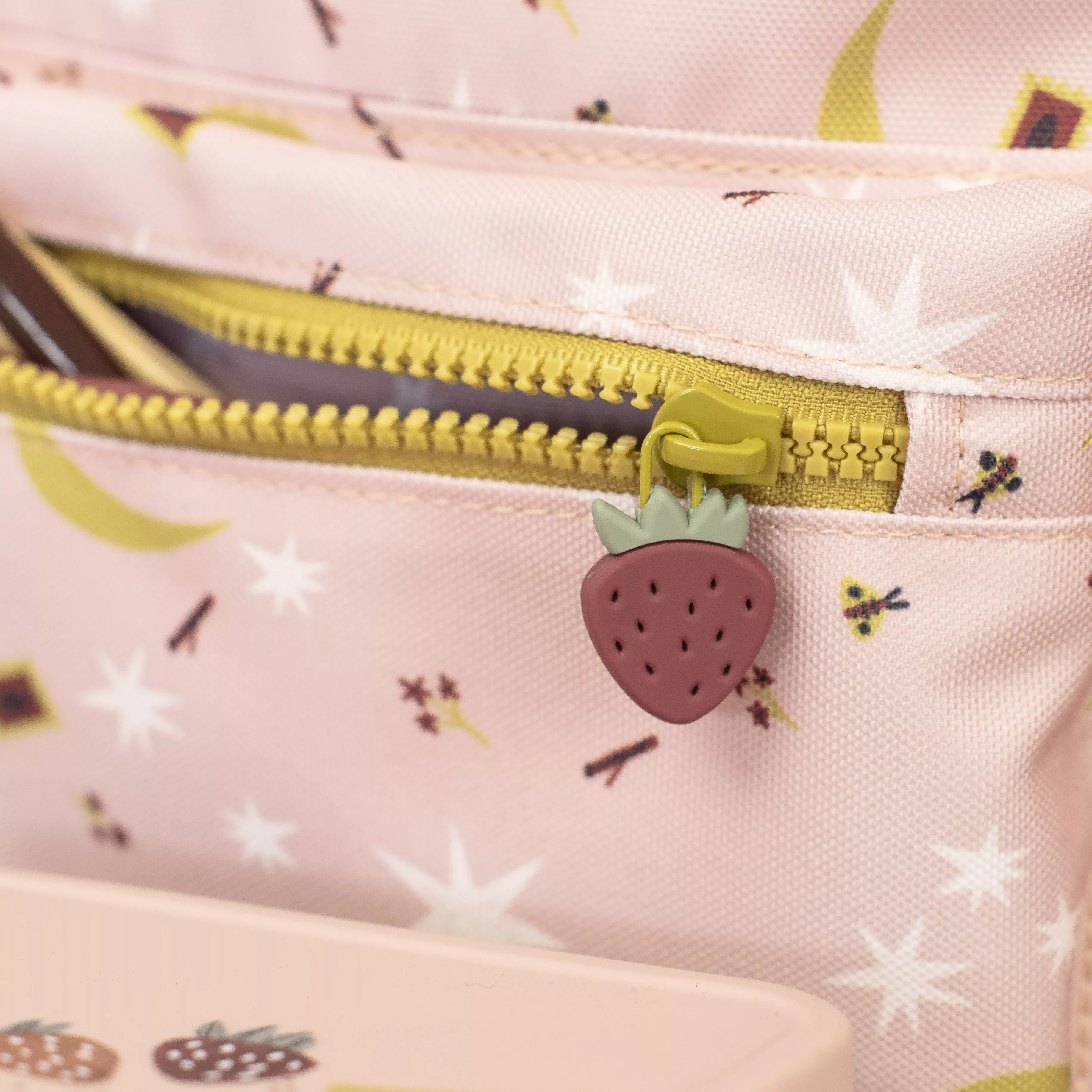 Close-up of a pink childrens backpack with a strawberry-shaped zipper pull and floral pattern.