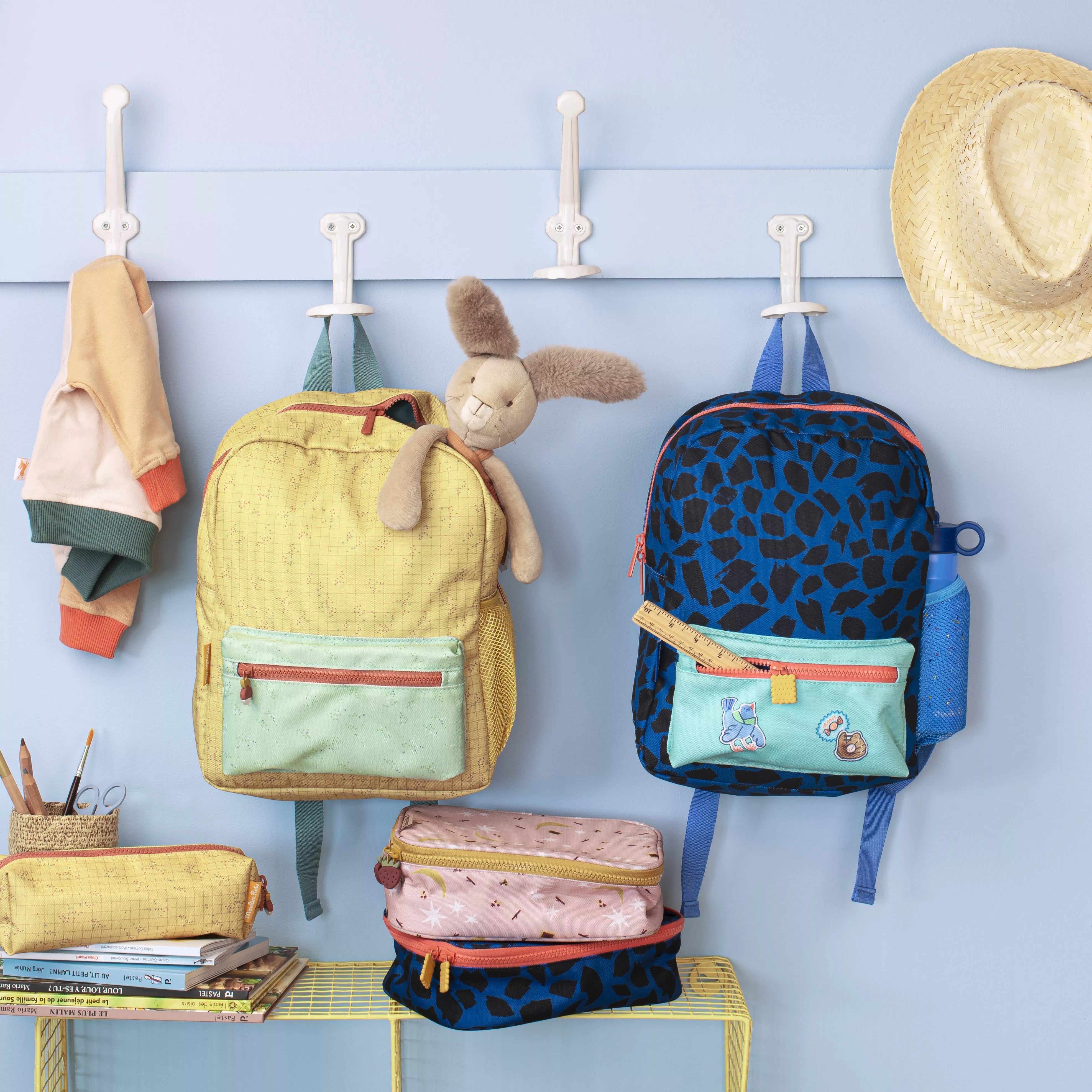 Colorful backpacks and accessories hanging on a wall with hooks.