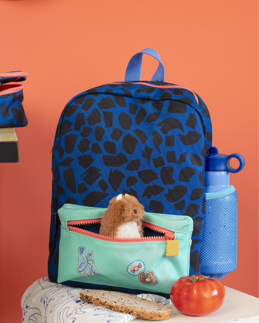 Blue backpack with black spots, a small bag with a toy, and a blue water bottle on an orange background.