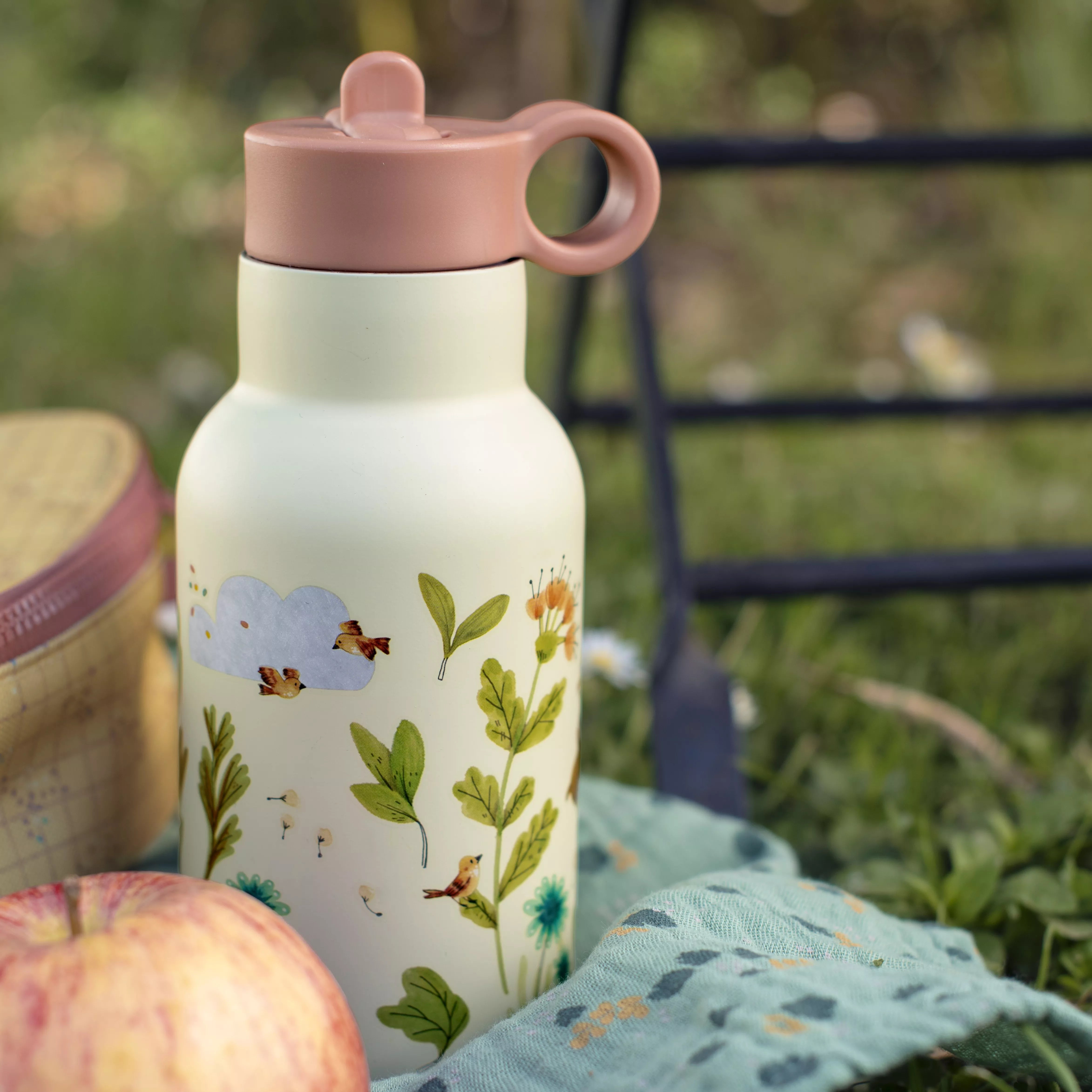 Floral-patterned water bottle with pink lid on a picnic blanket outdoors