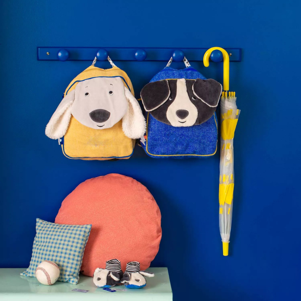moulin roty Children's backpackss on a blue wall with a blue shelf.