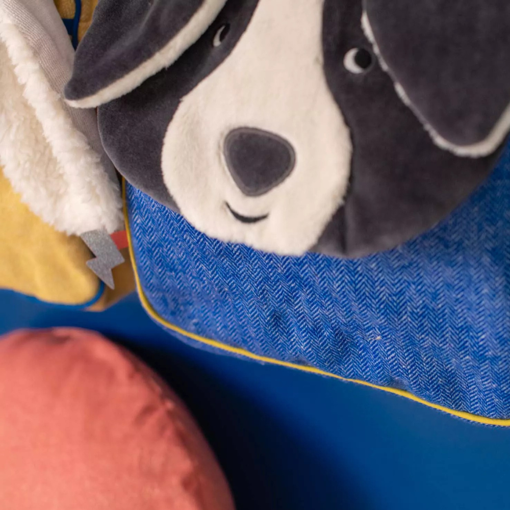 Close-up of a Moulin roty plush dog backpack with a blue background