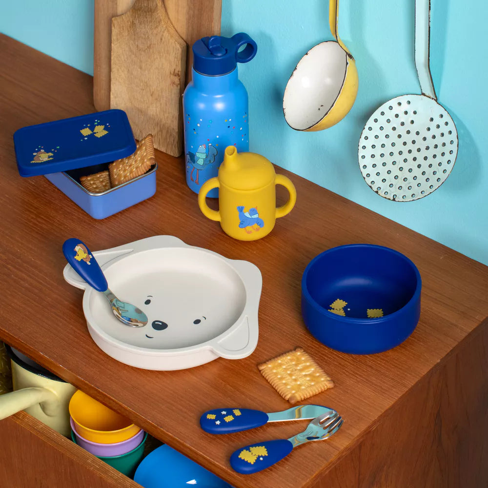 moulin roty puce and pilou Children's kitchenware set including bowls, spoons, and a cup on a wooden surface with a blue wall background.