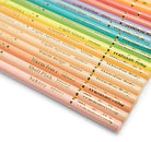 A close-up diagonal arrangement of pastel-colored wooden pencils with gold lettering on white barrels, showing shades from pale pink and peach through yellow, green, blue, and purple.