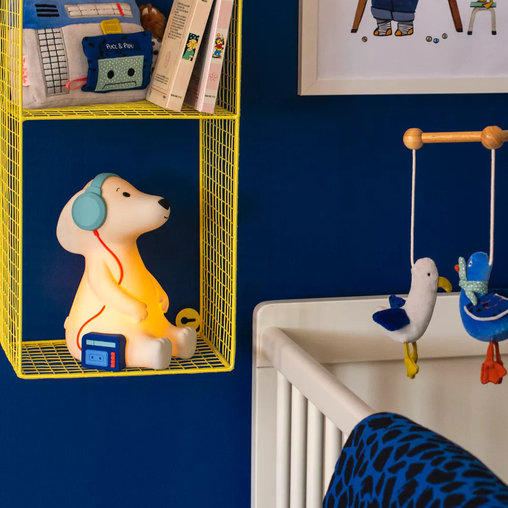 Children's room with a yellow shelf, dog shaped nightlight, and crib mobile against a blue wall.