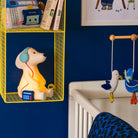 Children's room with a yellow shelf, dog shaped nightlight, and crib mobile against a blue wall.