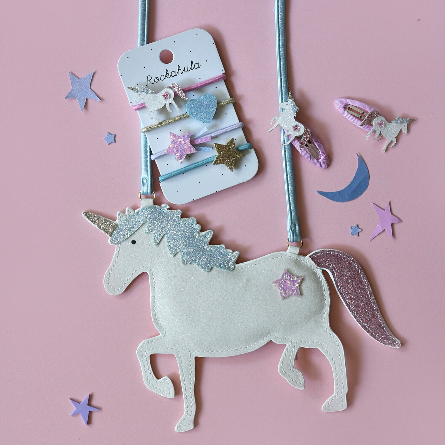 Unicorn-shaped hair clip on a pink background with decorative stars and clips.