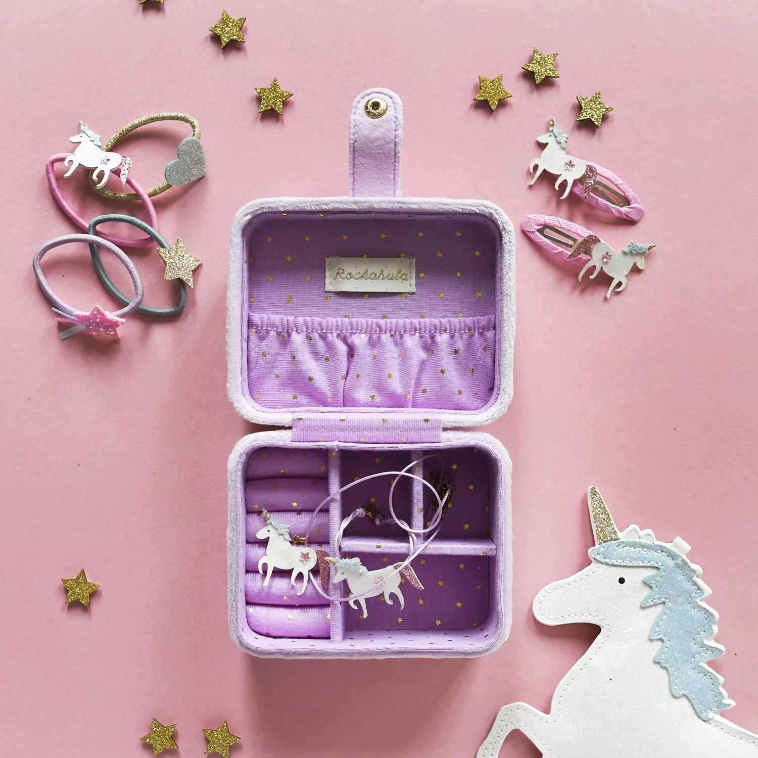 Purple jewelry case with unicorn-themed accessories on a pink background