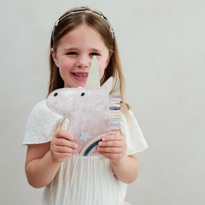 Young girl holding a velvet unicorn handbag against a plain background