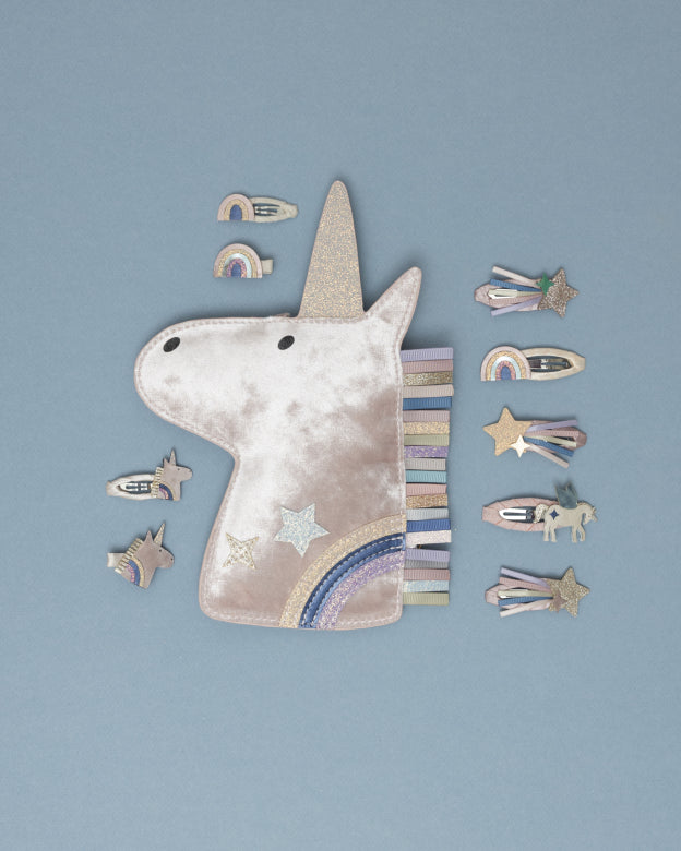 Unicorn-shaped handbag with a strap and unicorn hair clips on a blue background