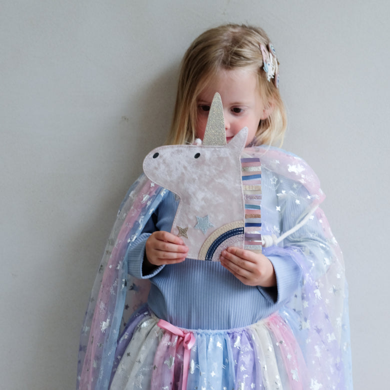 Child holding a unicorn-shaped handbag with a starry night design, wearing a colorful cape.