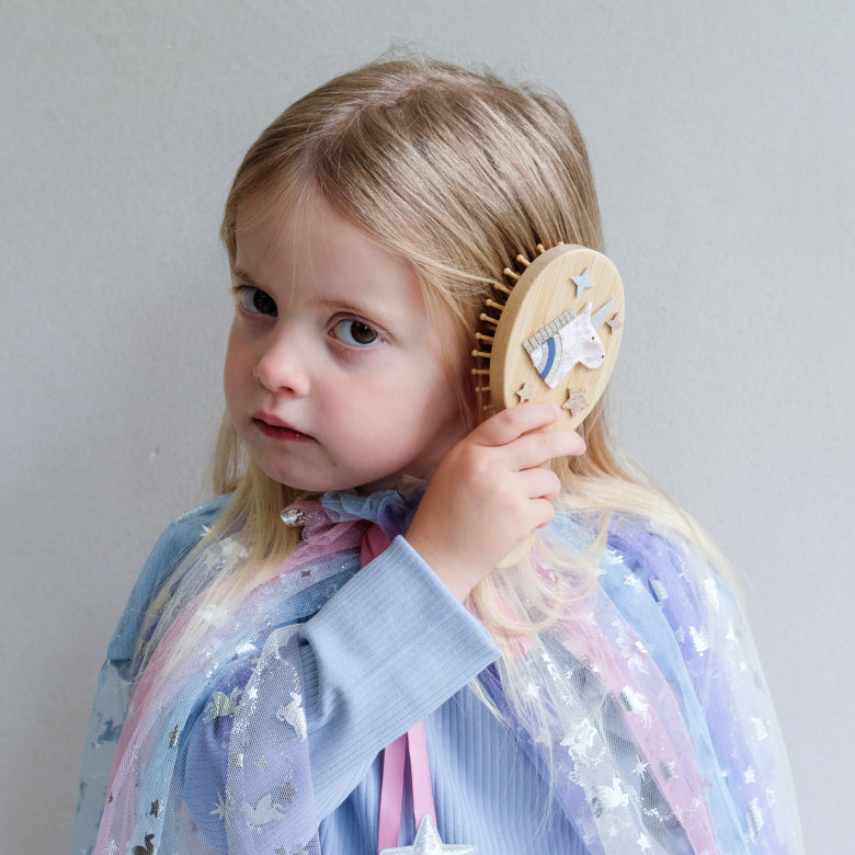 Child holding a wooden hairbrush with unicorn star designs against a plain background