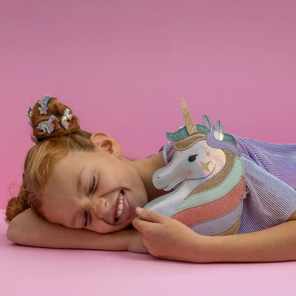 Child holding a unicorn plush toy against a pink background