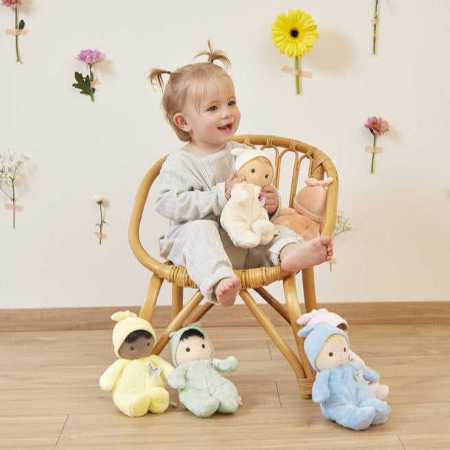 Child sitting in a chair with plush toys in a room with decorative flowers on the wall.