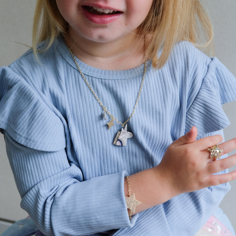 Child wearing a blue sweater with  unicorn jewelry including a necklace, bracelet, and ring.
