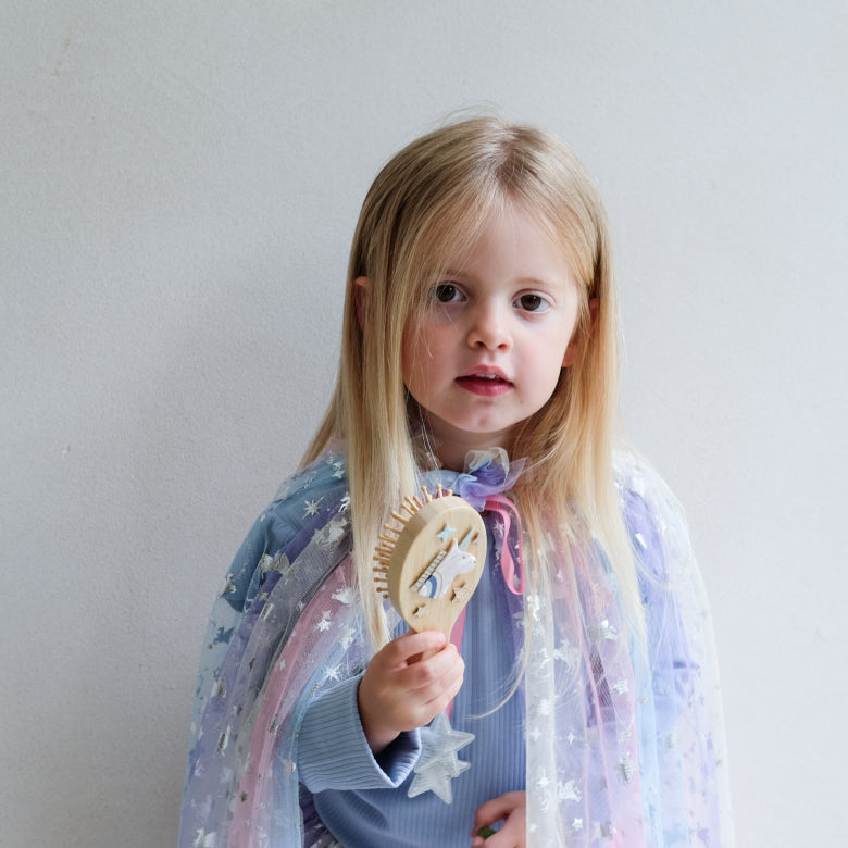 Young girl holding a wooden hairbrush with a star and unicorn design against a plain background