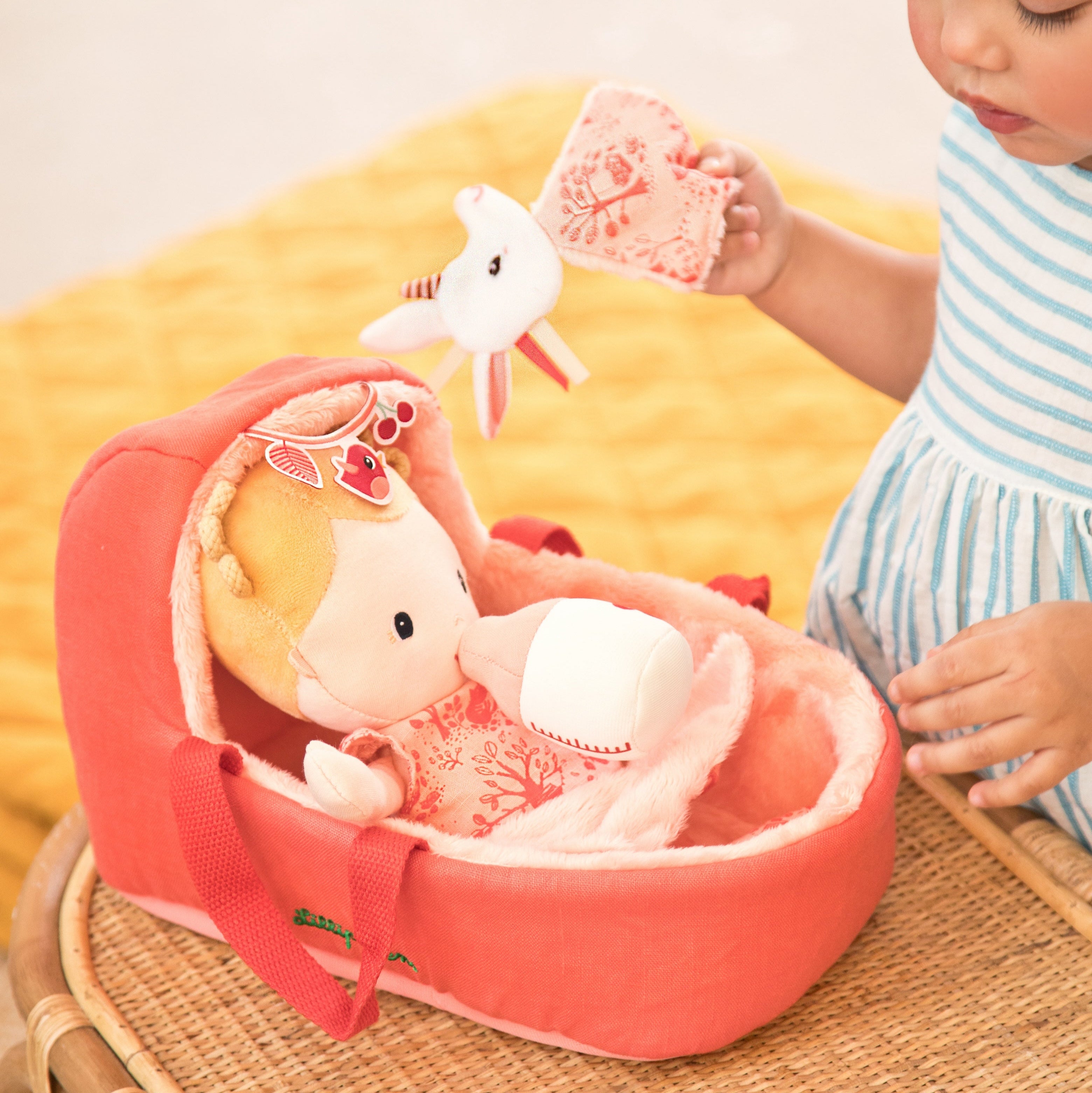 Child playing with a baby dolly in a pink bassinet on a yellow blanket