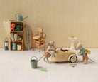 A styled miniature toy scene featuring two mouse figurines playing with a beige toy car, alongside a small bucket, lanterns, a chair, shelving, and other vintage-inspired accessories against a cream striped backdrop.