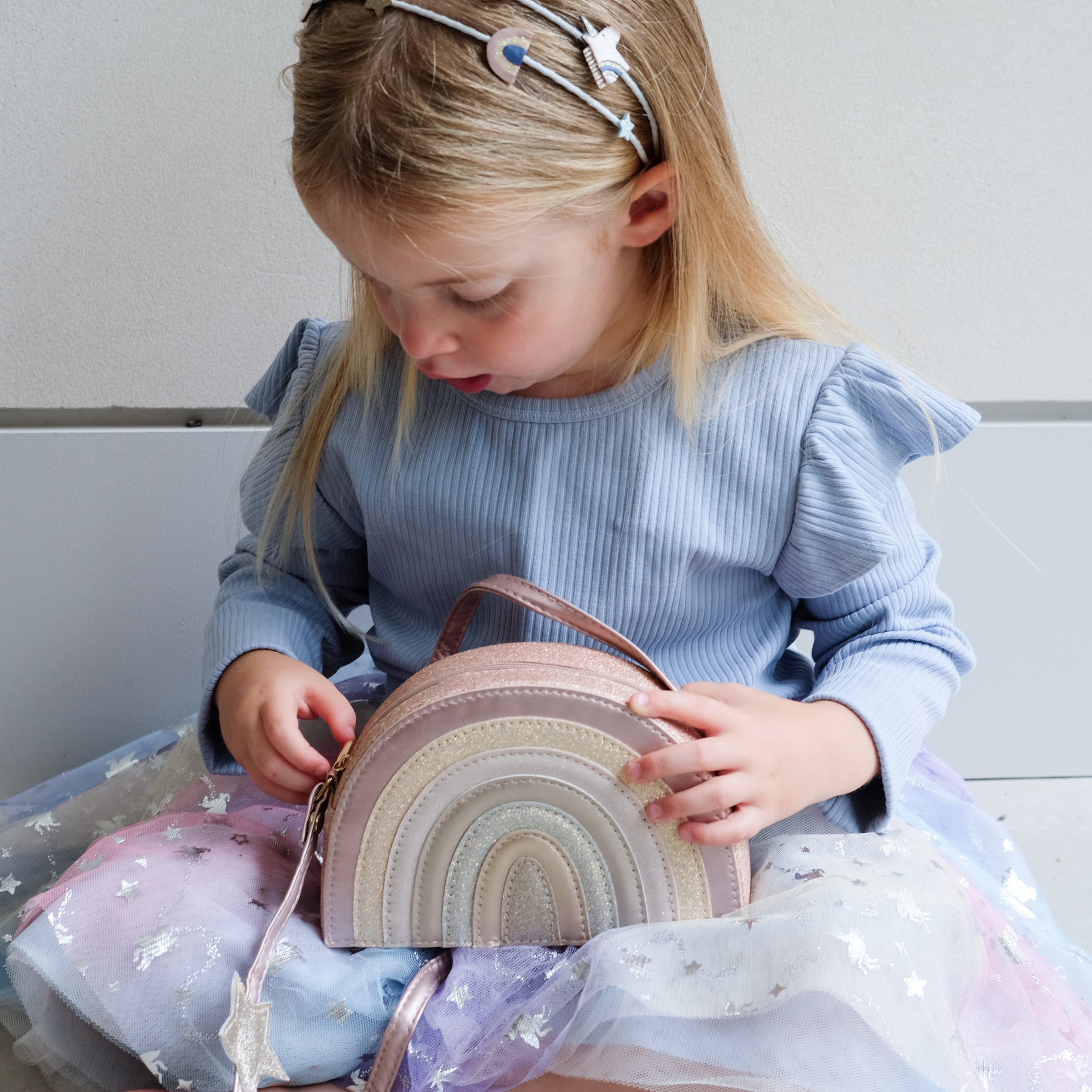 Young girl holding a pale pink rainbowd shaped bag with a plain background