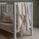 White crib with floral bedding and pillow against a neutral background