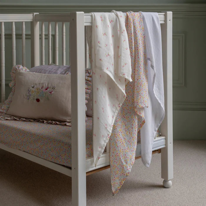 White crib with floral bedding and pillow against a neutral background