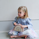 Young girl holding a rainbow-shaped bag against a plain background